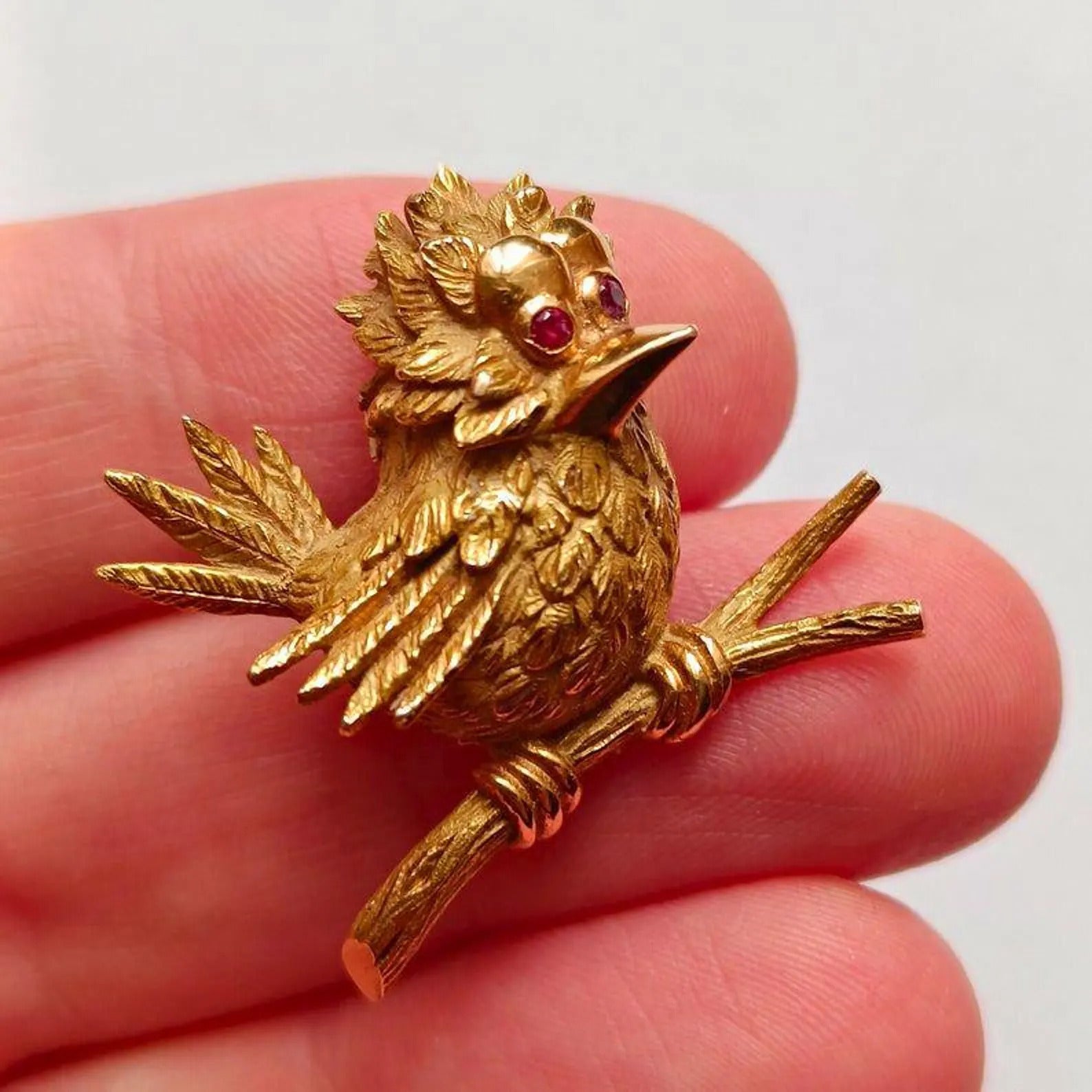 Gold bird brooch with red gemstones on a hand against a white background