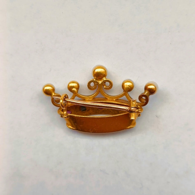 Gold crown-shaped brooch on a light gray background