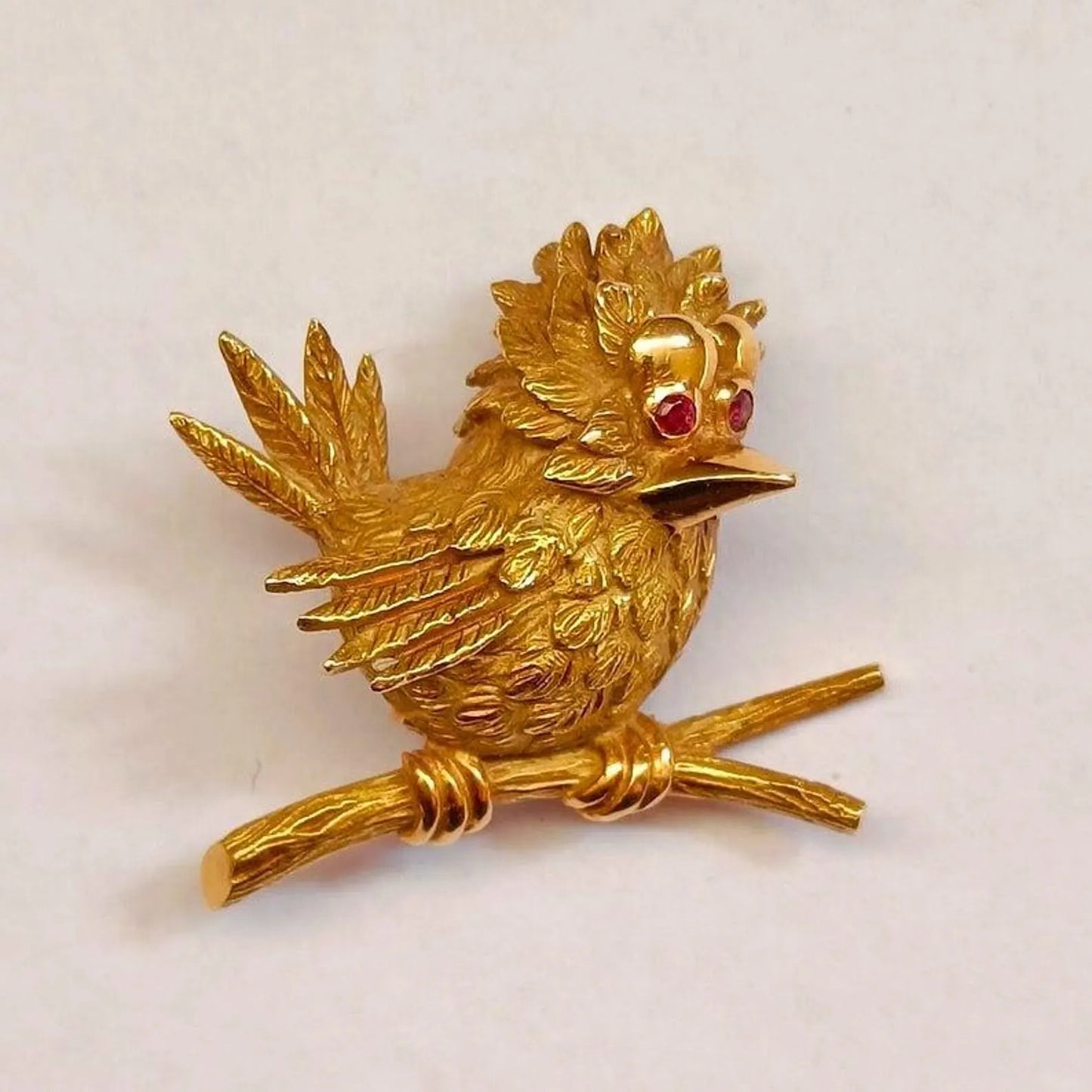 Gold bird brooch with red gemstones on a white background