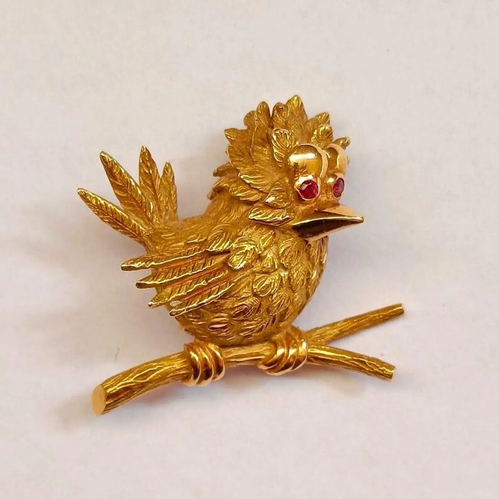 Gold bird brooch with red gemstones on a white background