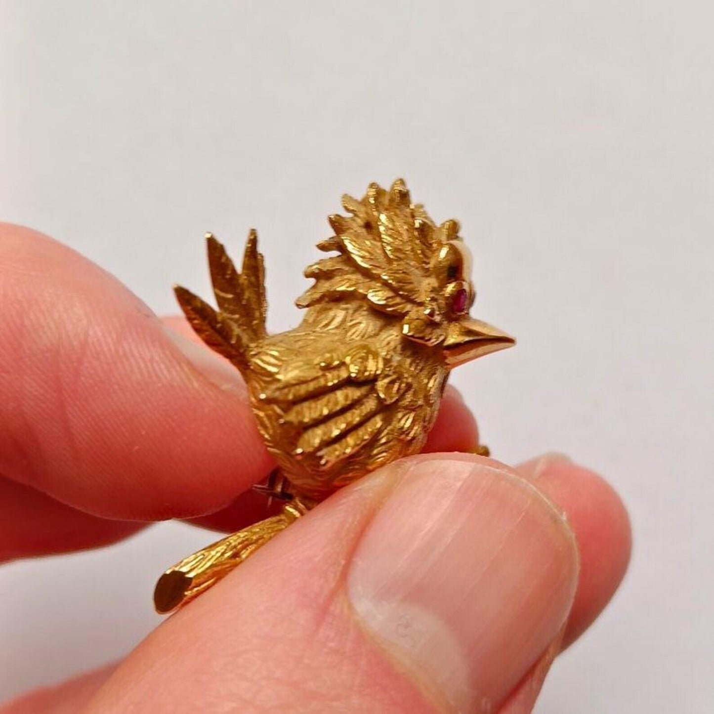 Gold bird figurine held between fingers against a plain background